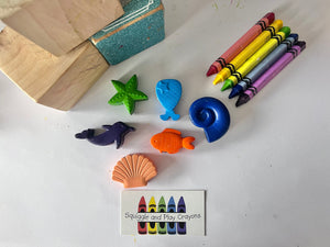 crayons in the shapes of a starfish, mermaids' tail, round cochlea seashell, dolphin, goldfish looking shape crayon and scallop seashell shaped crayon.