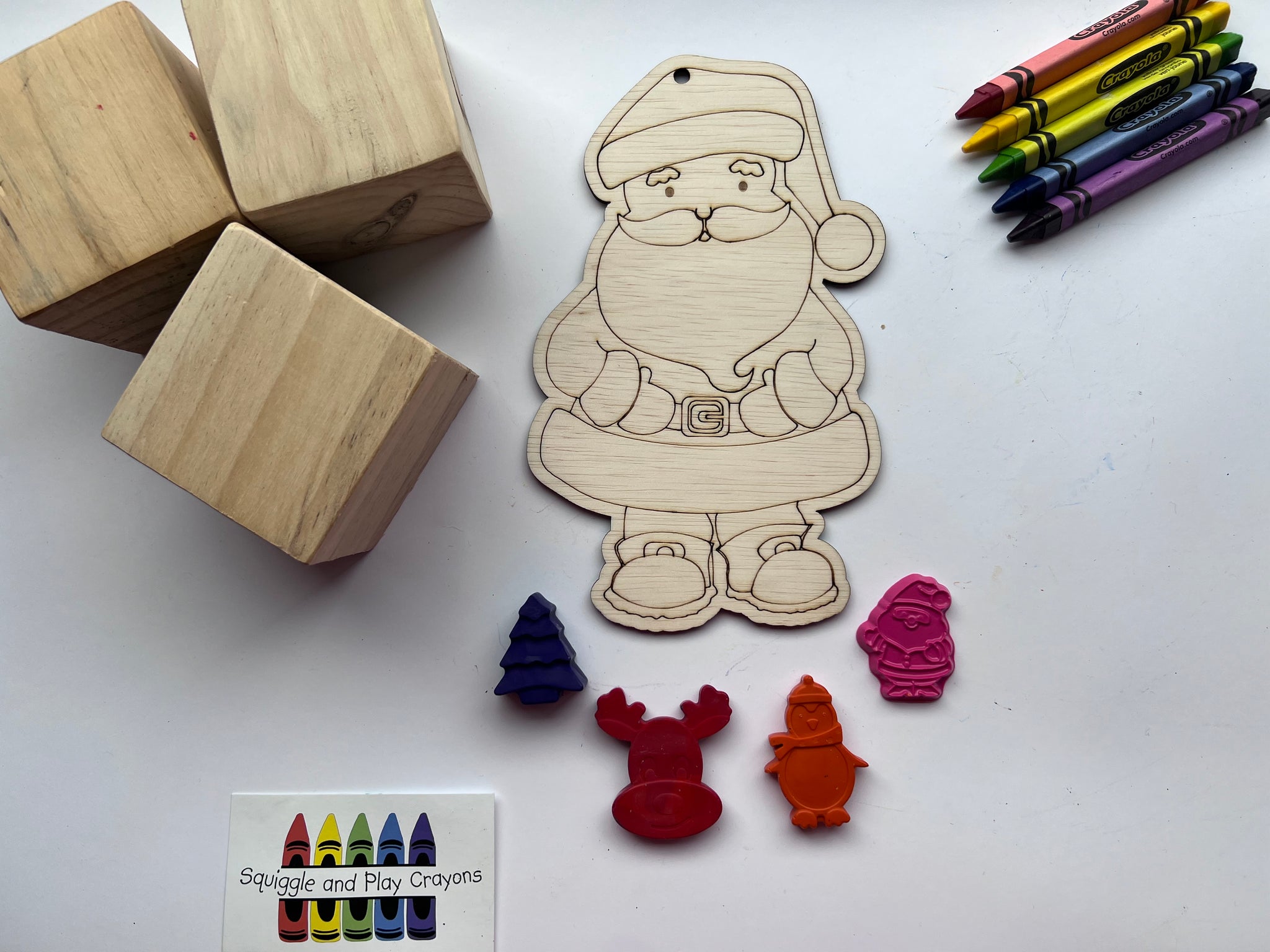 wooden cut out shaped in a Sant holding his belt. 4 Small crayons in the shape of a Christmas tree, head of a reindeer, standing penguin wearing a beanie and scarf, standing Sant