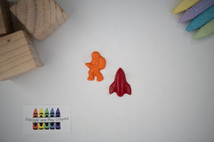 one rocket shaped crayon and one astronaut shaped crayon