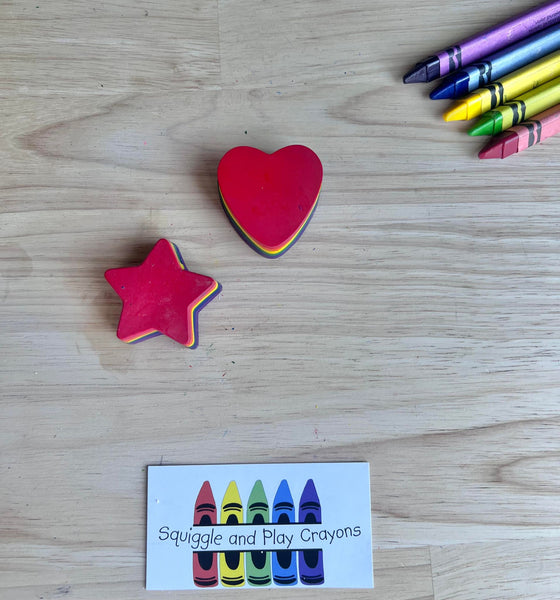 Star and heart-shaped crayons on a wooden surface with a 'Squiggle and Play Crayons' card.