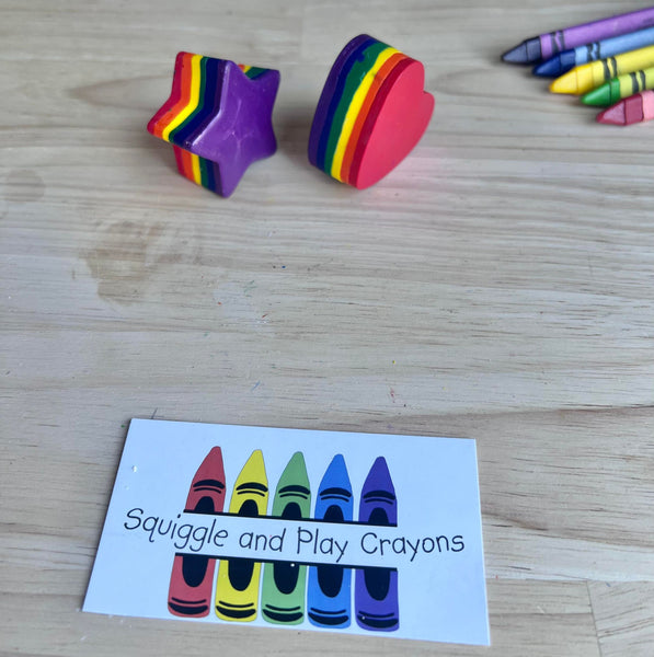 Colorful star-shaped crayons and heart-shaped crayon on a wooden surface with a card labeled 'Squiggle and Play Crayons'.