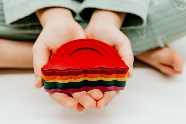 A child's hands holding a rainbow crayon