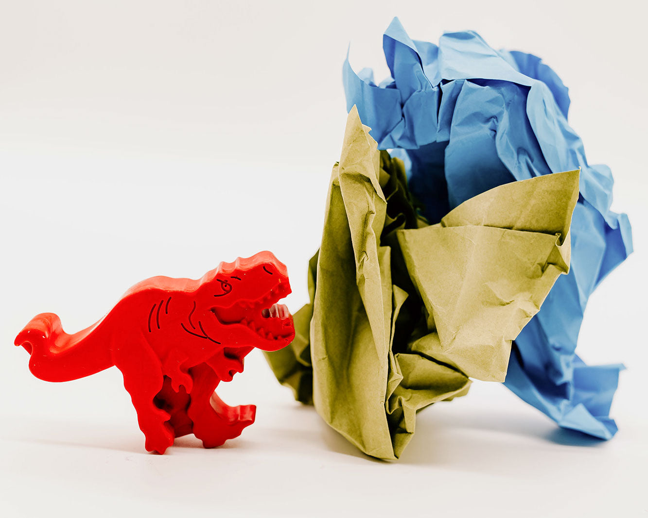 A large, red, realistic-looking 2D t-rex roaring at s ball of scrunched paper