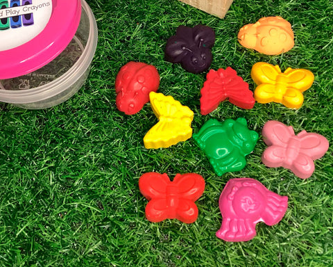 a neon-pink-lidded round tub next to a selection of crayons in the shape of garden creatures: bees, butterflies, ladybirds, frogs, and spiders