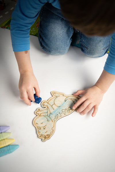 A child colours in a wooden dinosaur shape with a blue crayon