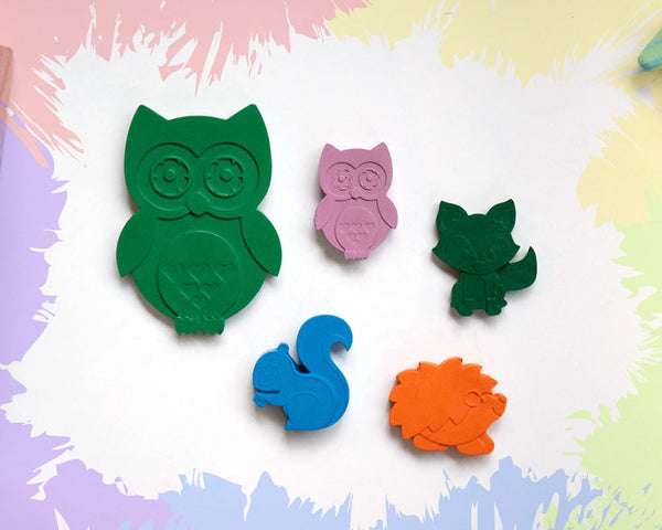 A large, green owl crayon, with 4 small crayons in the shape of a fox, a hedgehog, an owl, and a squirrel