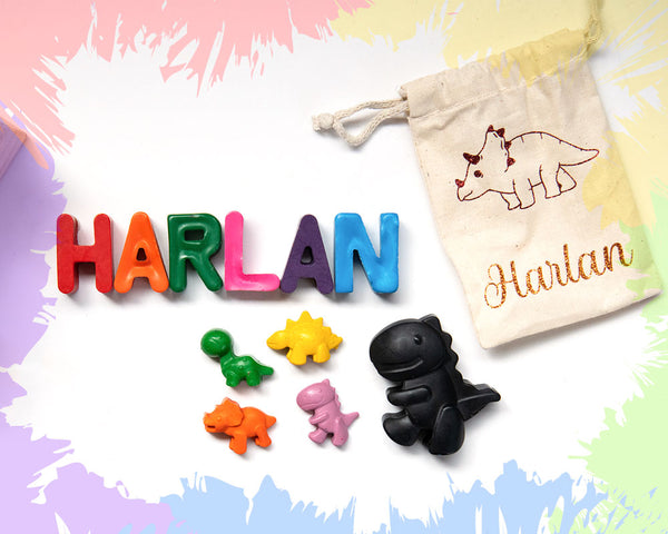 letter-shaped crayons spelling Harlan, a large cartoon t-rex dinosaur crayon with 4 smaller dinosaurs, and a calico drawstring bag with an outlined stegosaurus and the name Harlan in glittery cursive text